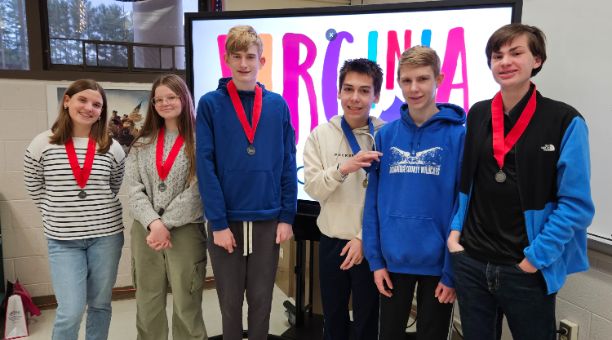  Six teenagers wearing medals stand in a classroom in front of a screen displaying the word "VIRGINI